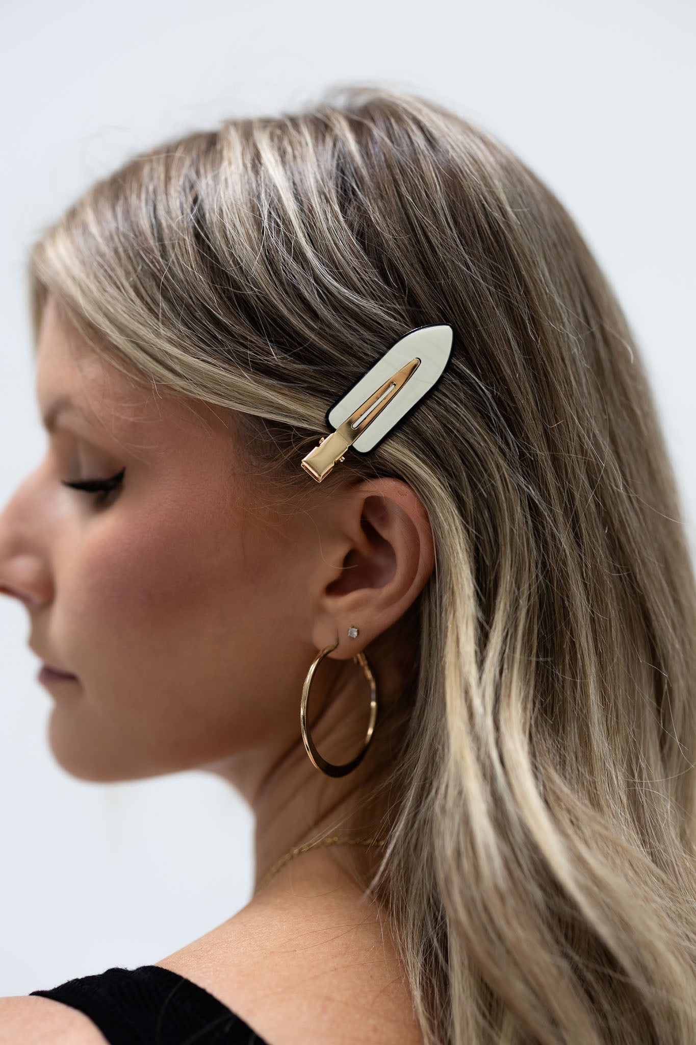 Woman wearing a hair extension clip with a white base and gold accents.