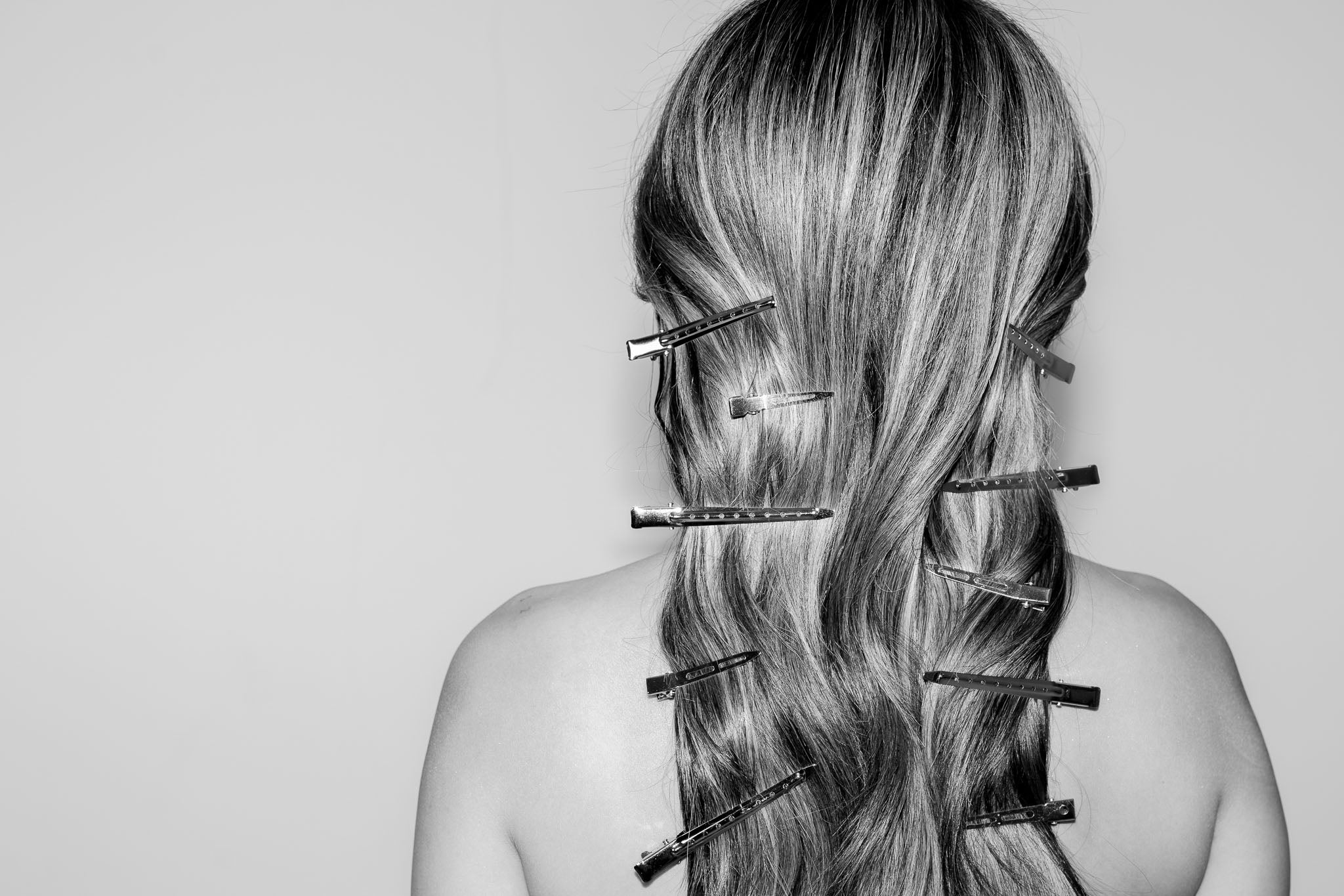 Person with hair styled in a ponytail using hair clips on a plain background
