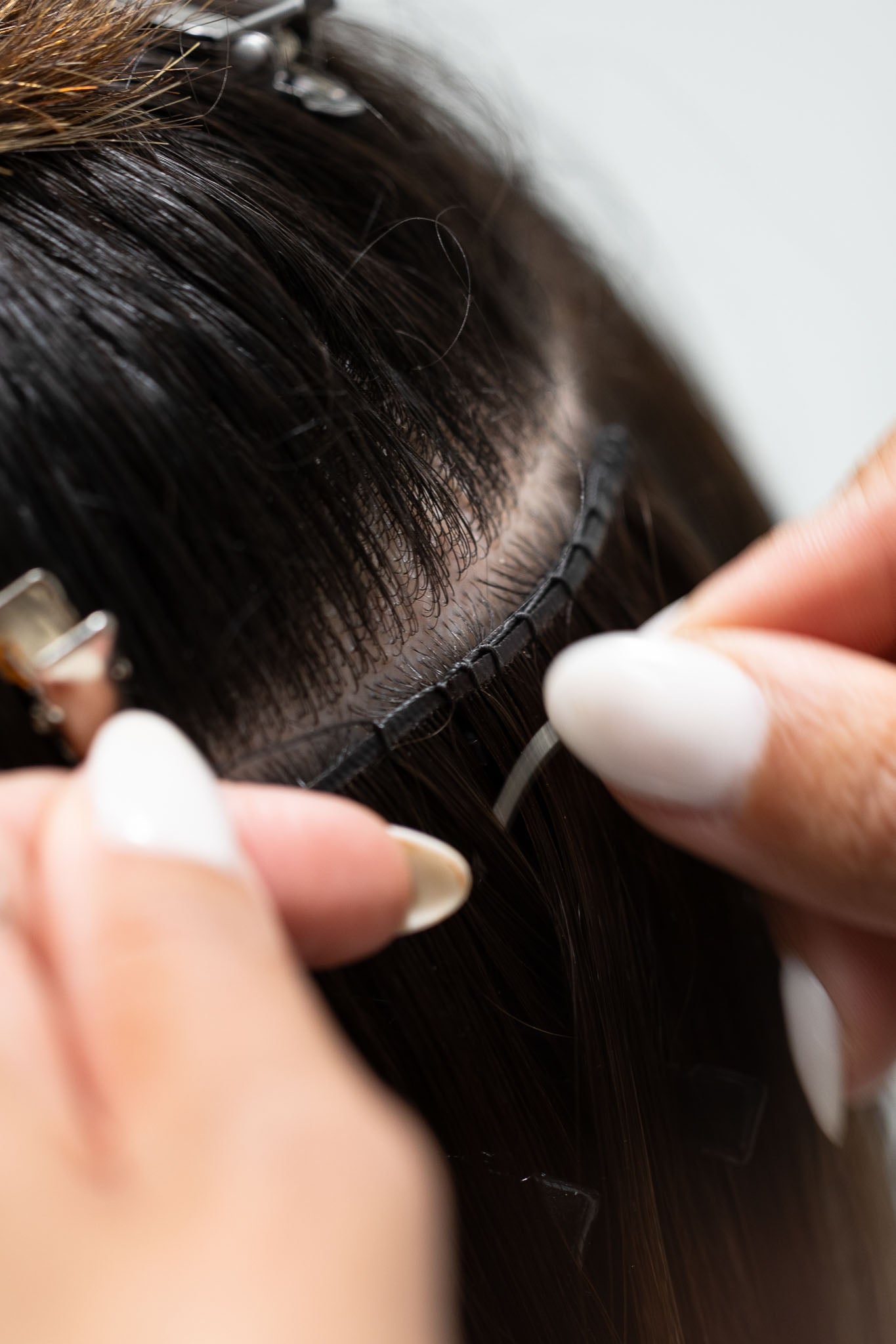 Close-up of a person's hands working on a hair extension with a blurred background