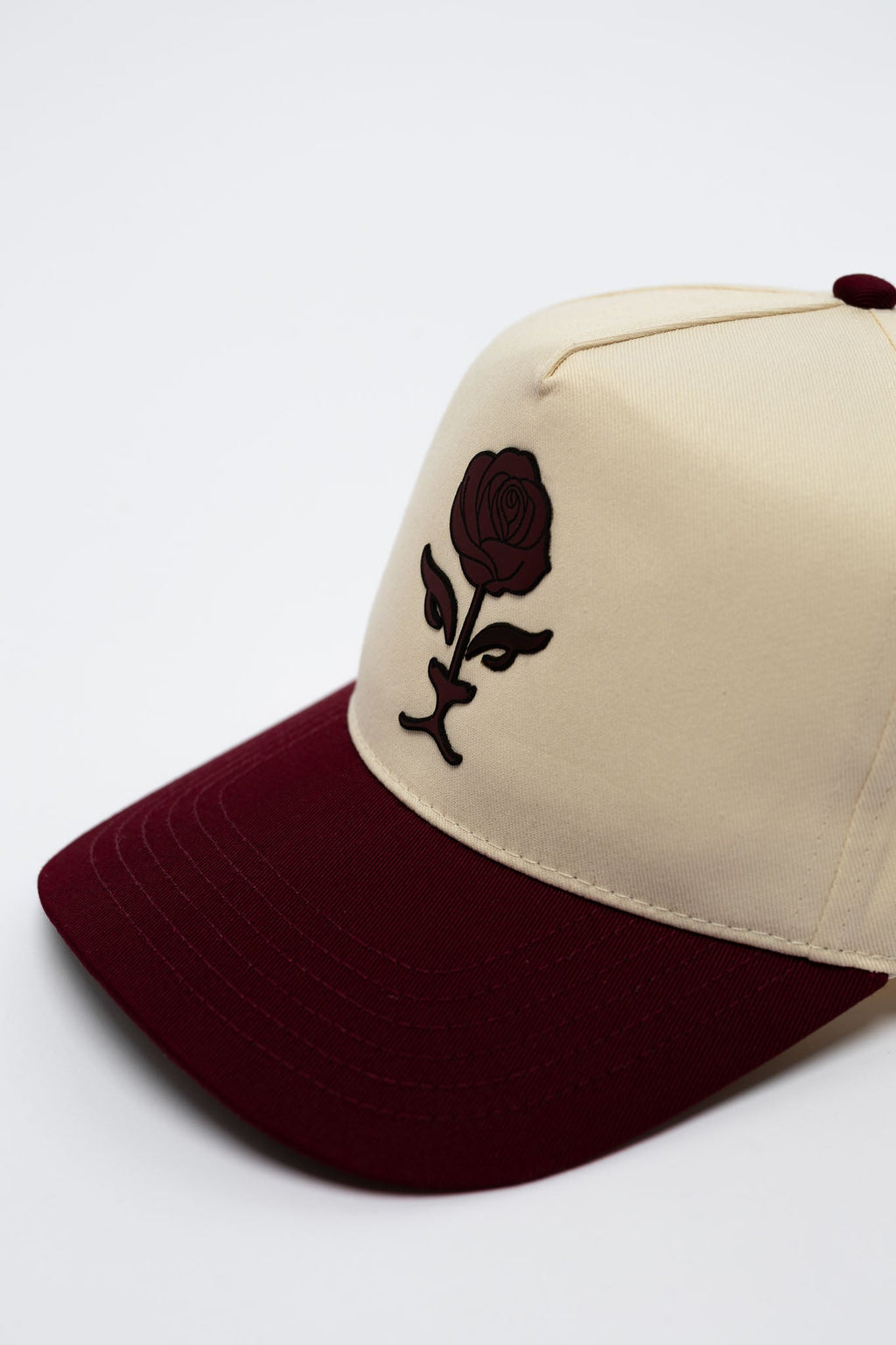 Beige and maroon cap with a black logo on a light gray background