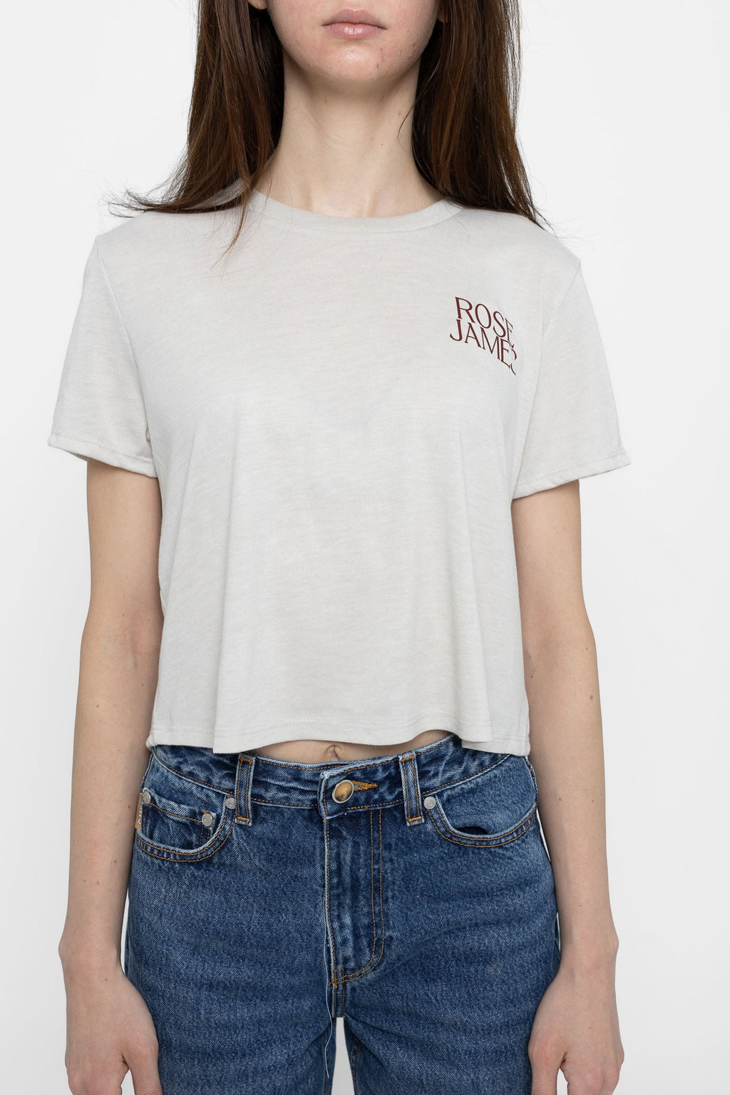 Person wearing a white t-shirt with 'ROSE JAMES' logo and blue jeans on a white background