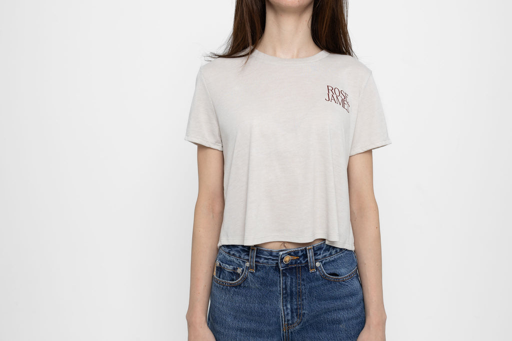 Person wearing a beige t-shirt with a logo and blue jeans on a white background