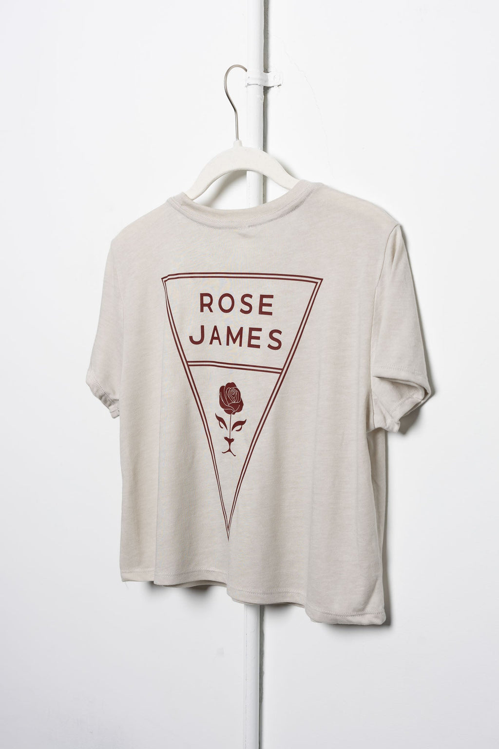 Beige t-shirt with 'Rose James' logo on a white hanger against a white background