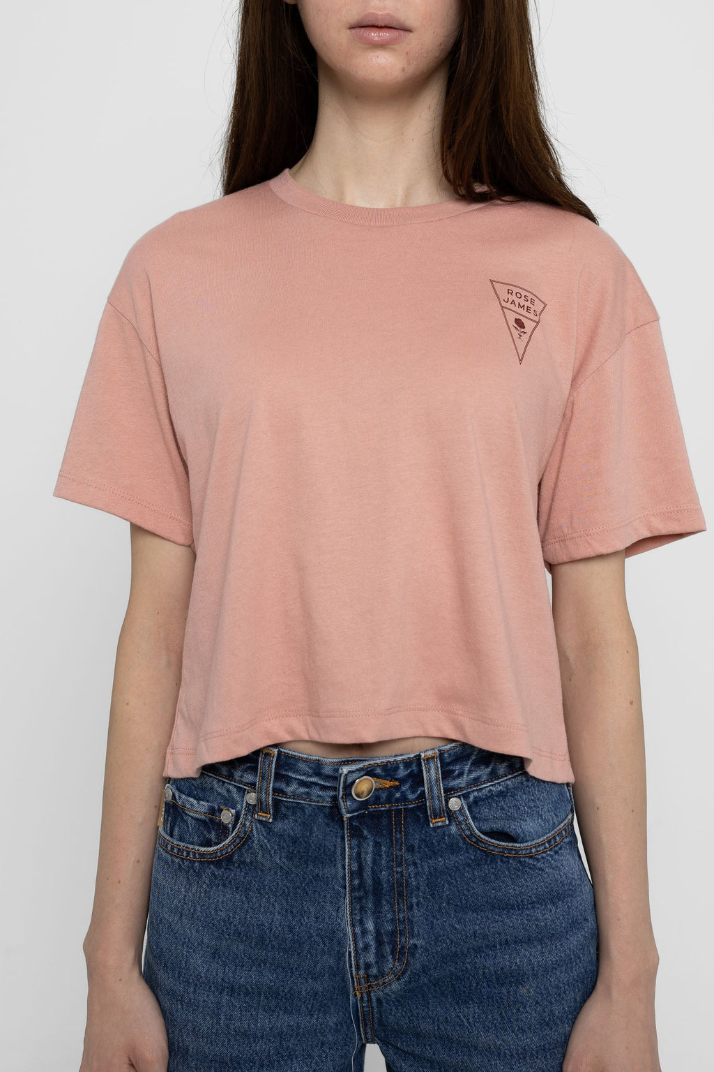 Person wearing a pink t-shirt with a logo and blue jeans on a white background