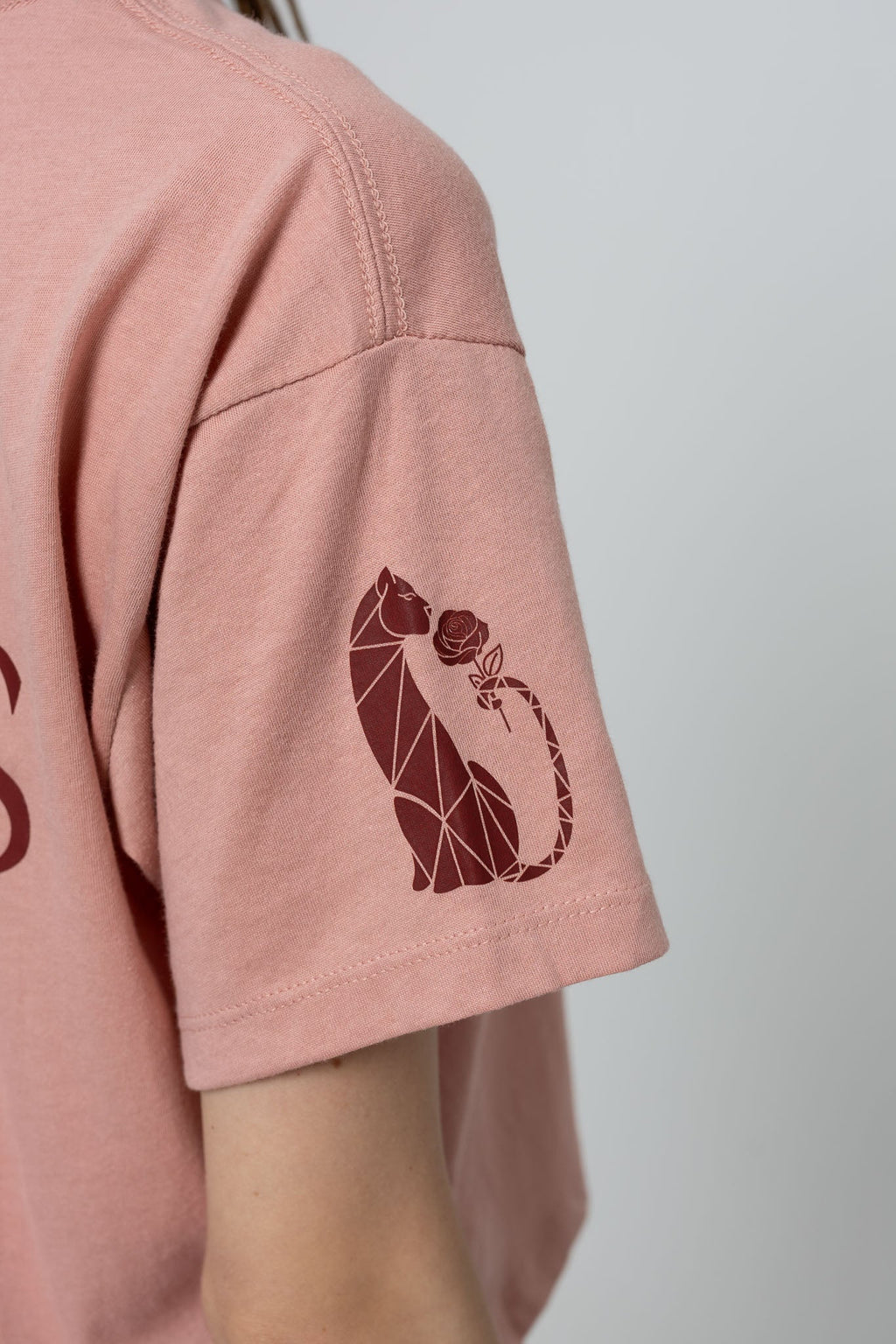 Pink t-shirt with a geometric cat design on the sleeve against a plain background