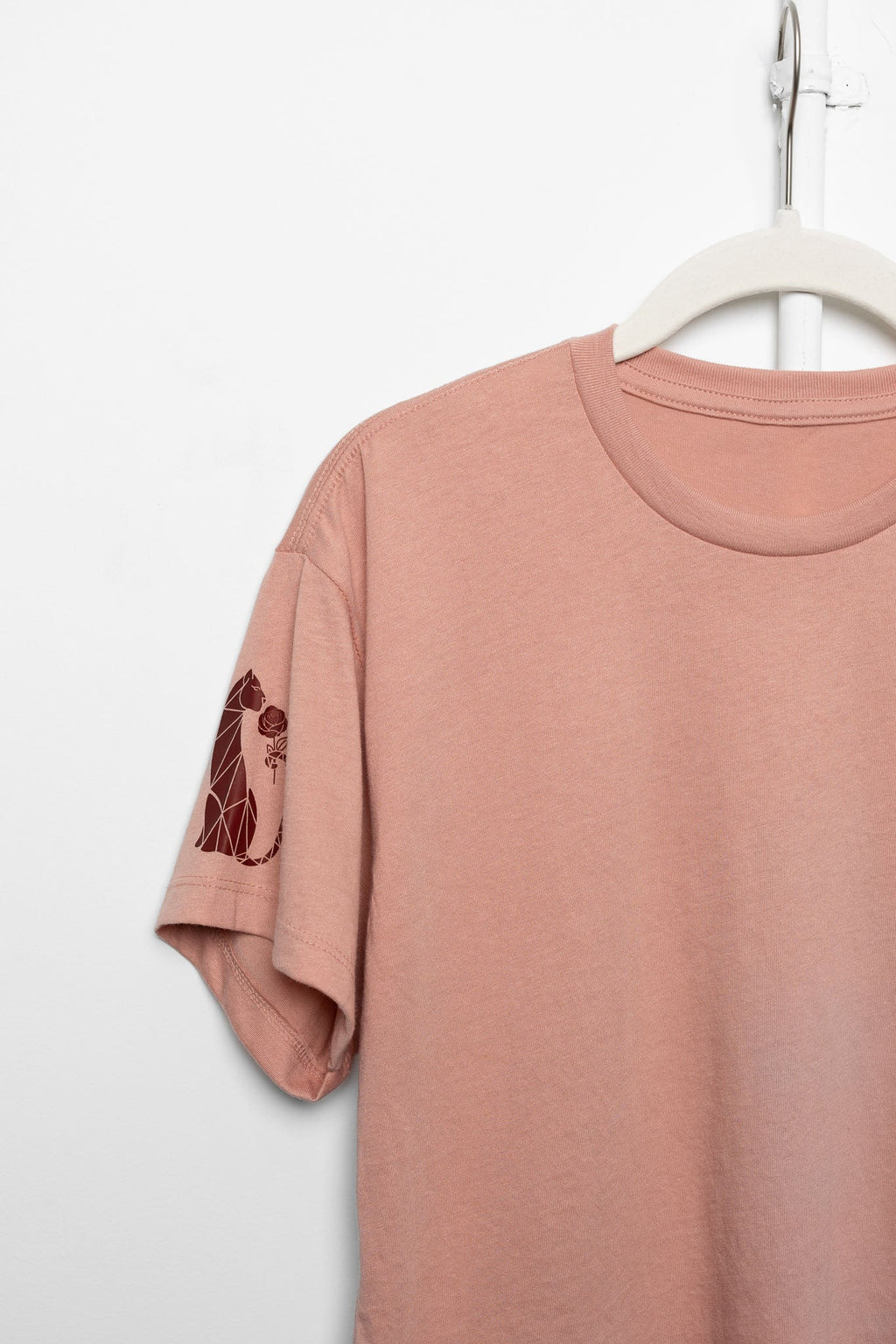 Pink t-shirt with a design on the sleeve hanging on a white hanger against a white background