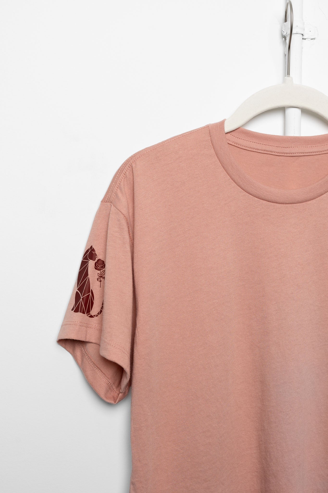 Pink t-shirt with a design on the sleeve hanging on a white hanger against a white background